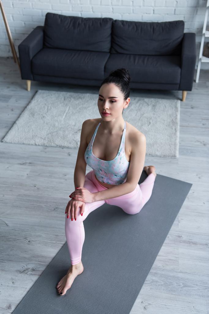 Hochwinkelaufnahme einer barfüßigen Frau, die Ausfallschritt auf Knien übt, posiert auf Yogamatte - Foto, Bild