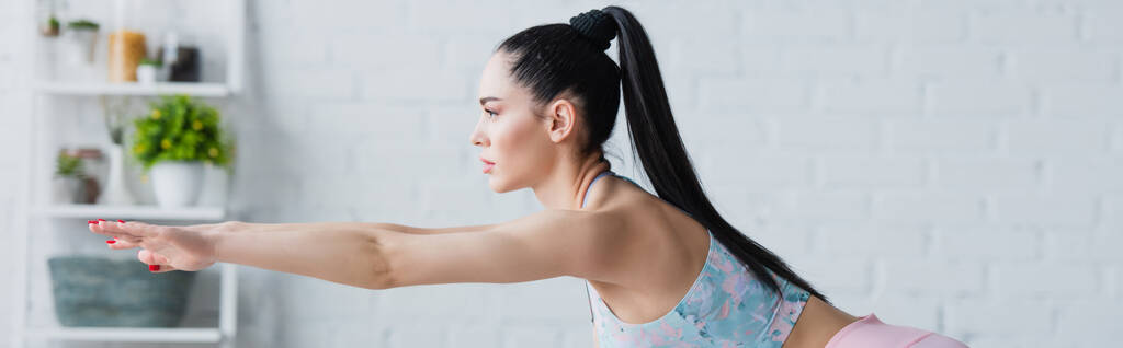 Вид сбоку брюнетки, тренирующейся с протянутыми руками, баннер - Фото, изображение