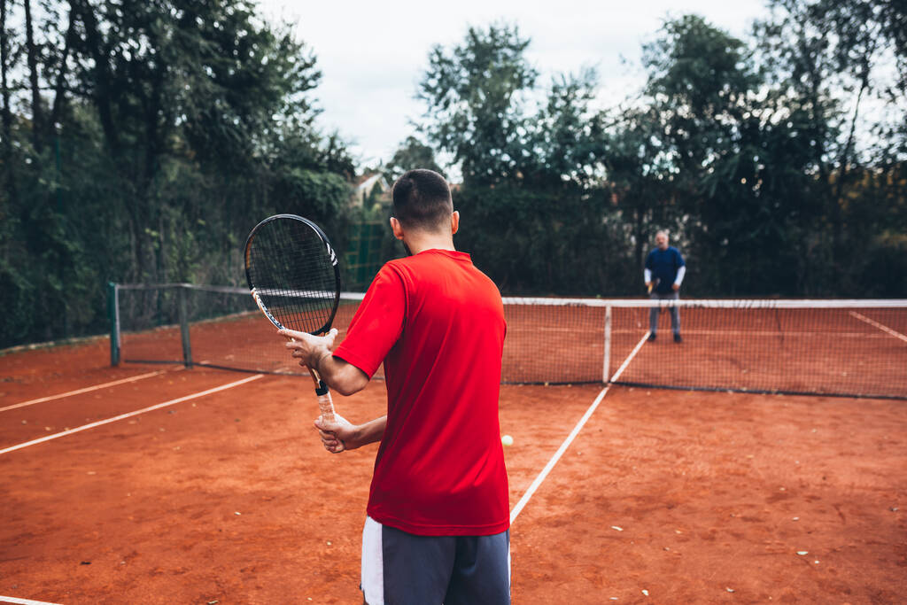 человек играет в теннис на открытом воздухе на глиняном корте - Фото, изображение