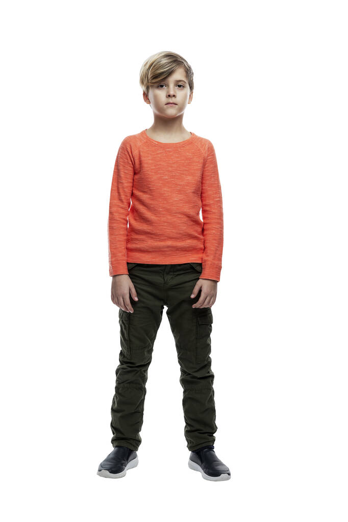 オレンジのジャケットとジーンズに身を包んだ9歳の少年が立っている。高さは？。白い背景に隔離されている。垂直. - 写真・画像