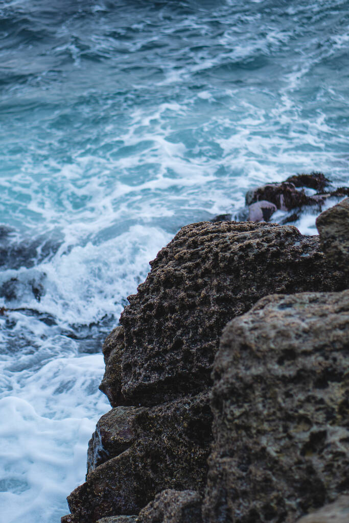 Um tiro vertical de um penhasco rochoso com ondas no fundo - Foto, Imagem