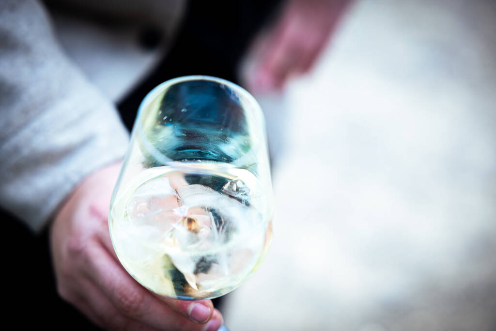Bulanık arka planda bir bardak beyaz şarap tutan bir el. - Fotoğraf, Görsel