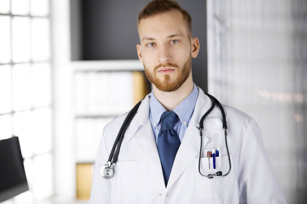 Rudovousý doktor stojí přímo na klinice poblíž jeho pracoviště. Portrét lékaře. Léky, zdravotní péče - Fotografie, Obrázek
