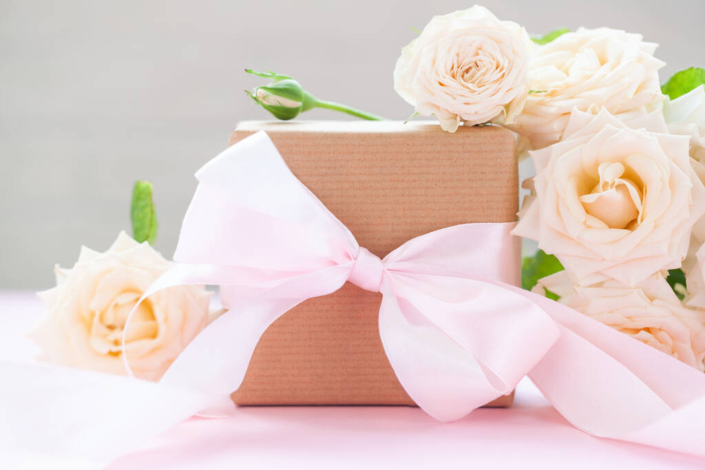 Caja de regalo envuelta en papel marrón con rosas rosadas sobre fondo rosa. Tarjeta de felicitación. - Foto, Imagen