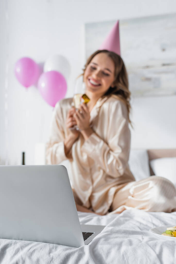 Laptop lähellä hymyilevä nainen juhlii syntymäpäivää hämärtynyt tausta makuuhuoneessa  - Valokuva, kuva