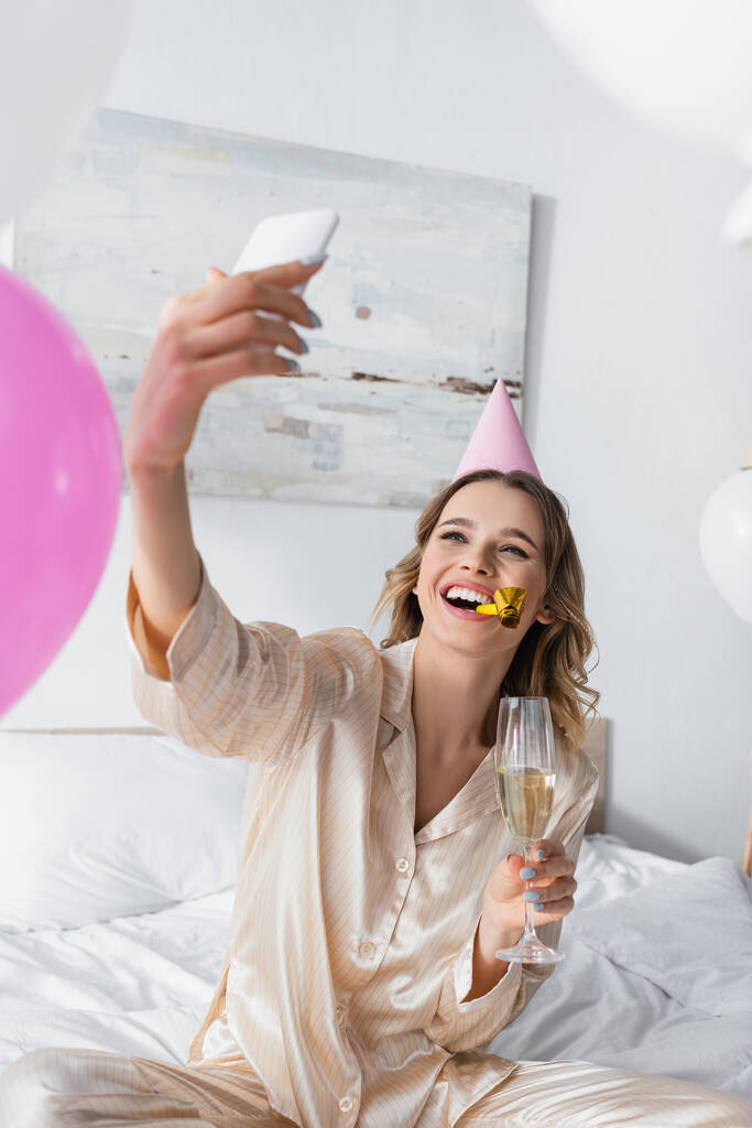 Улыбающаяся женщина с шампанским делает селфи на дне рождения дома  - Фото, изображение