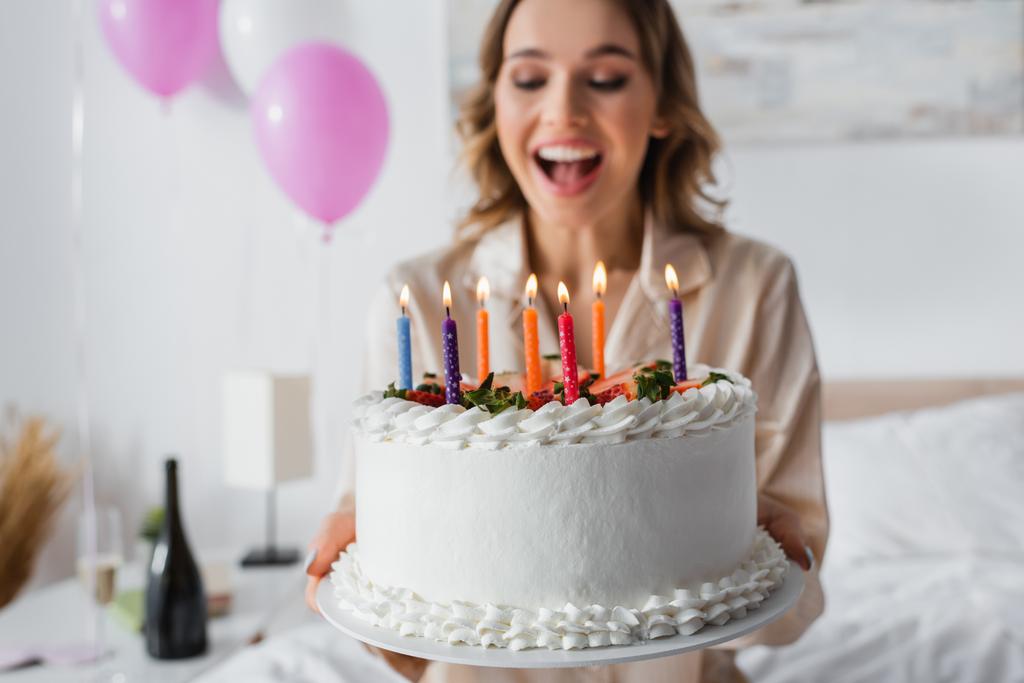 Tort urodzinowy w rękach podekscytowanej kobiety na rozmytym tle w sypialni  - Zdjęcie, obraz