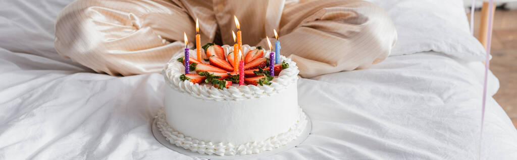 Oříznutý pohled na narozeninový dort se svíčkami v blízkosti ženy na posteli, banner  - Fotografie, Obrázek