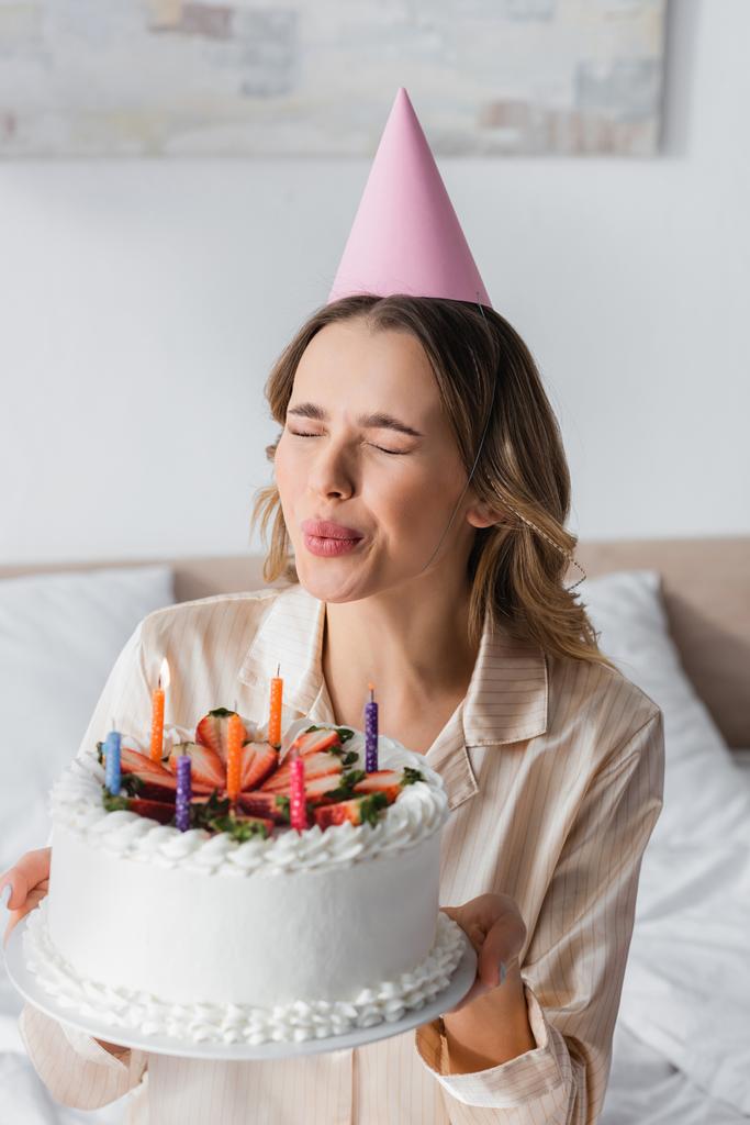 Kobieta w piżamie i czepek na imprezę zdmuchuje świeczki na torcie urodzinowym  - Zdjęcie, obraz