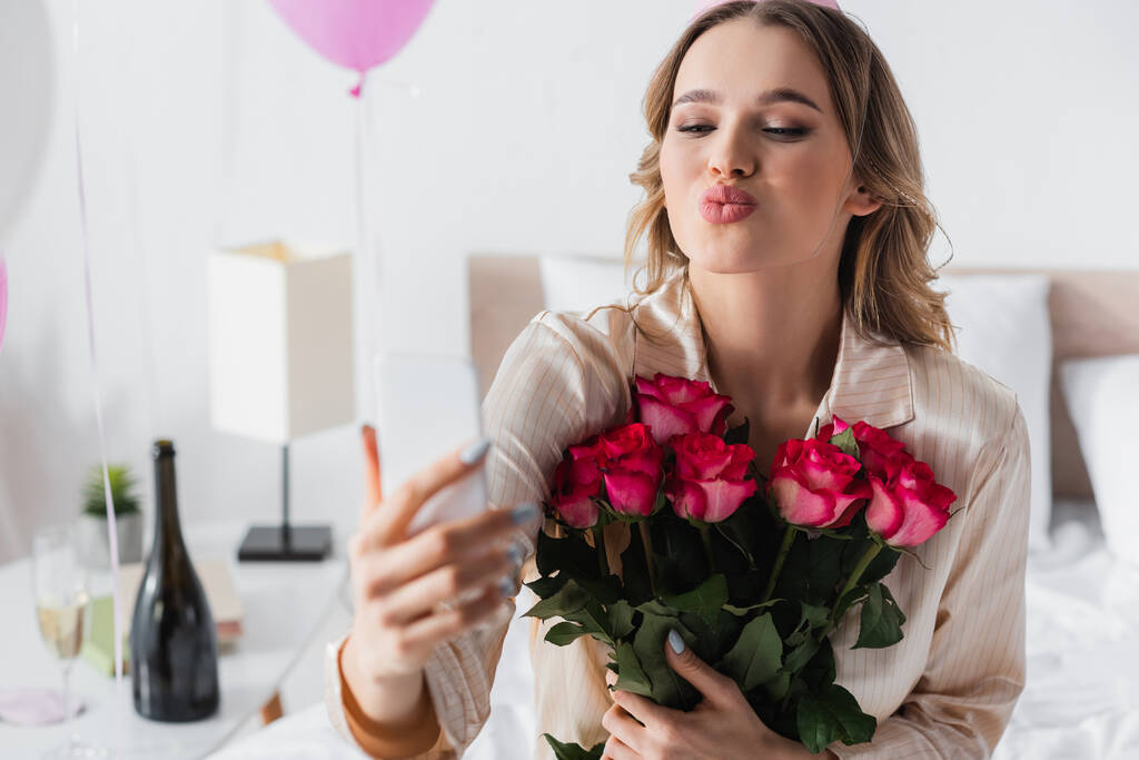Donna con rose scattare selfie su smartphone e labbra pouting a casa  - Foto, immagini