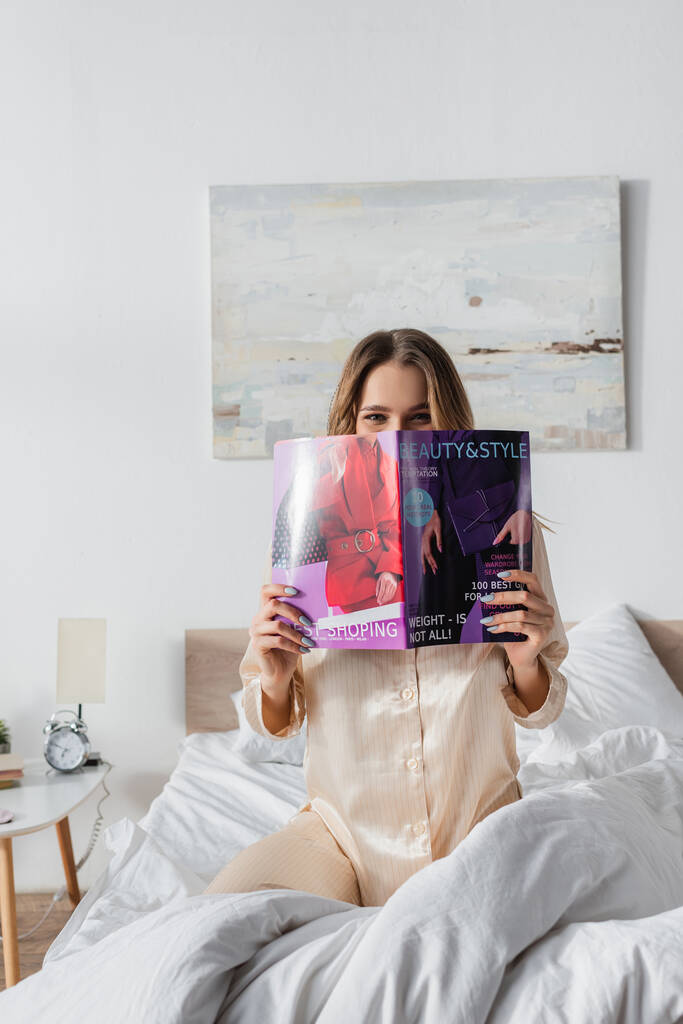 Žena zakrývající tvář s časopisem na posteli  - Fotografie, Obrázek