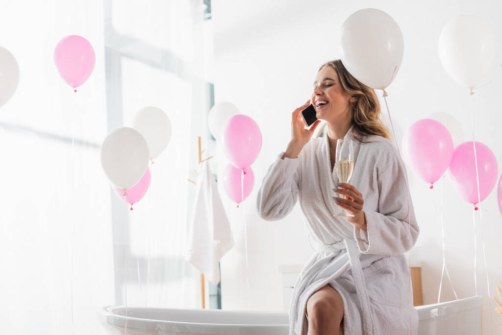 Усміхнена жінка в халаті говорить на смартфоні і тримає шампанське у ванній
  - Фото, зображення