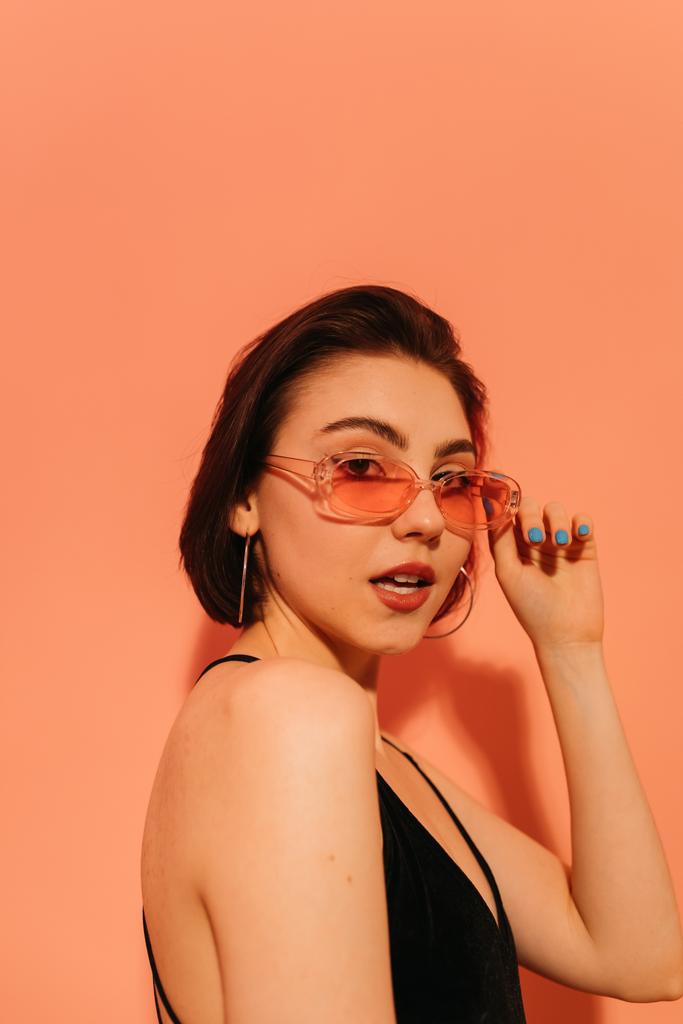 young woman in sunglasses with half-opened mouth on orange background - Photo, Image