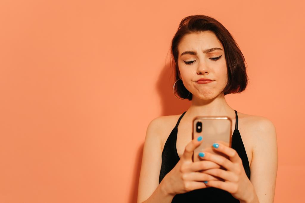 jeune femme regardant smartphone dans les mains sur fond orange - Photo, image