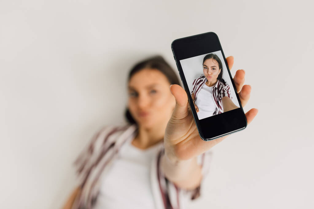 Smartphone mit Selfie-Bild einer jungen Frau mit Entengesicht-Fratze auf verschwommenem Hintergrund - Foto, Bild
