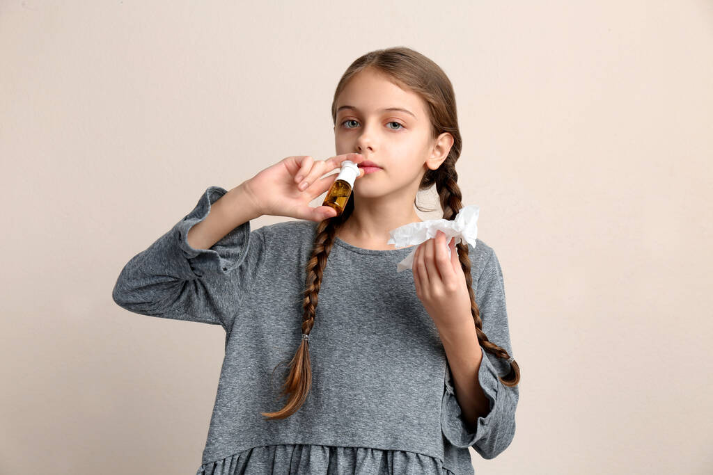 Menina doente usando spray nasal no fundo bege - Foto, Imagem