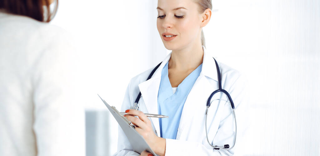 Vrouw - arts raadpleegt haar vrouwelijke patiënt tijdens het gebruik van klembord en medicatie geschiedenis record. Geneesmiddelenconcept - Foto, afbeelding