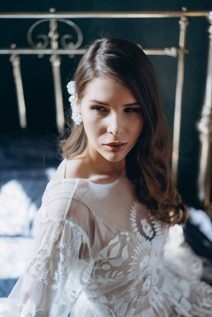 ragazza in un bellissimo bianco bohemien sensuale abito floreale seduto sul letto in luci e ombre e guardando la fotocamera  - Foto, immagini