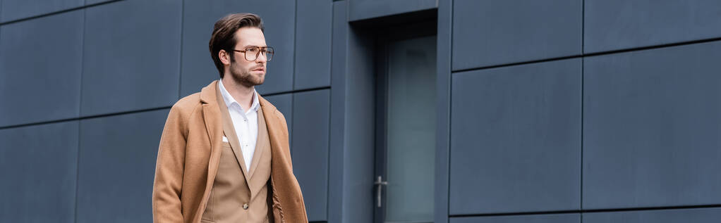 homme d'affaires barbu en lunettes et manteau beige marchant à l'extérieur, bannière - Photo, image