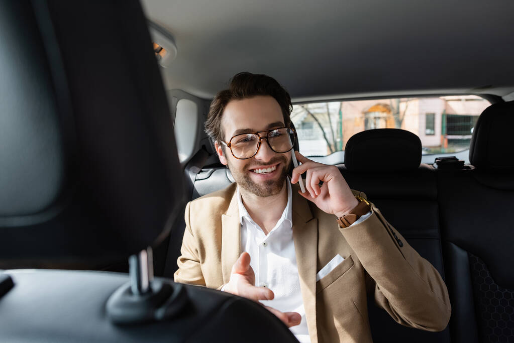 веселий чоловік в костюмі і окулярах розмовляє на смартфоні в машині
  - Фото, зображення
