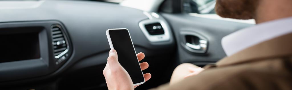 обрезанный вид размытого человека, держащего смартфон с пустым экраном в машине, баннер - Фото, изображение