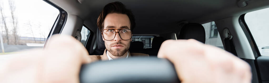 uomo barbuto in occhiali con le mani sul volante con primo piano sfocato, striscione - Foto, immagini