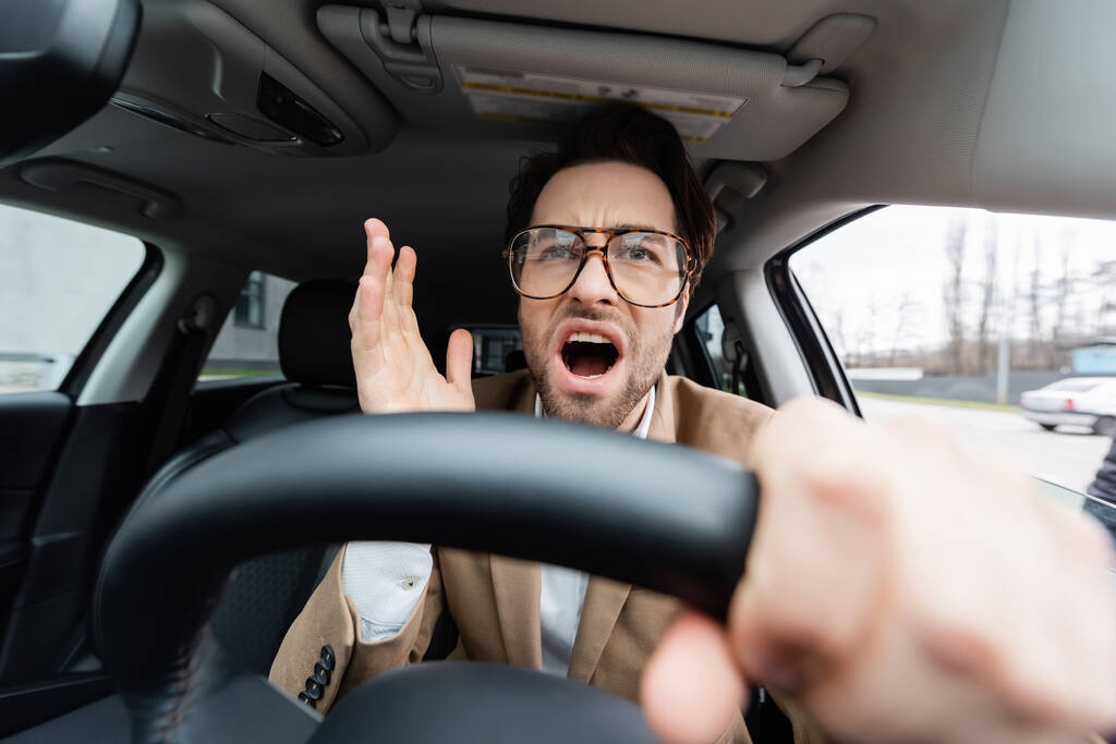 hombre disgustado en gafas con las manos en el volante con el primer plano borroso  - Foto, Imagen