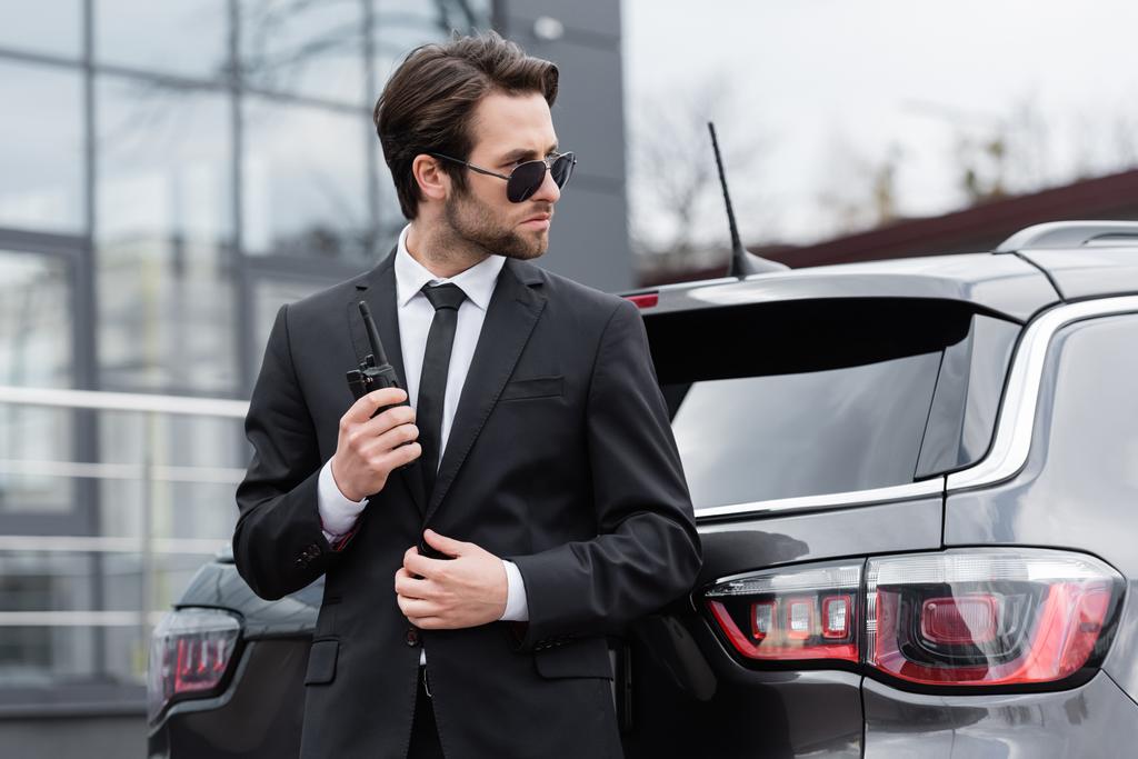 side view of bodyguard in sunglasses holding walkie talkie near modern car - Φωτογραφία, εικόνα