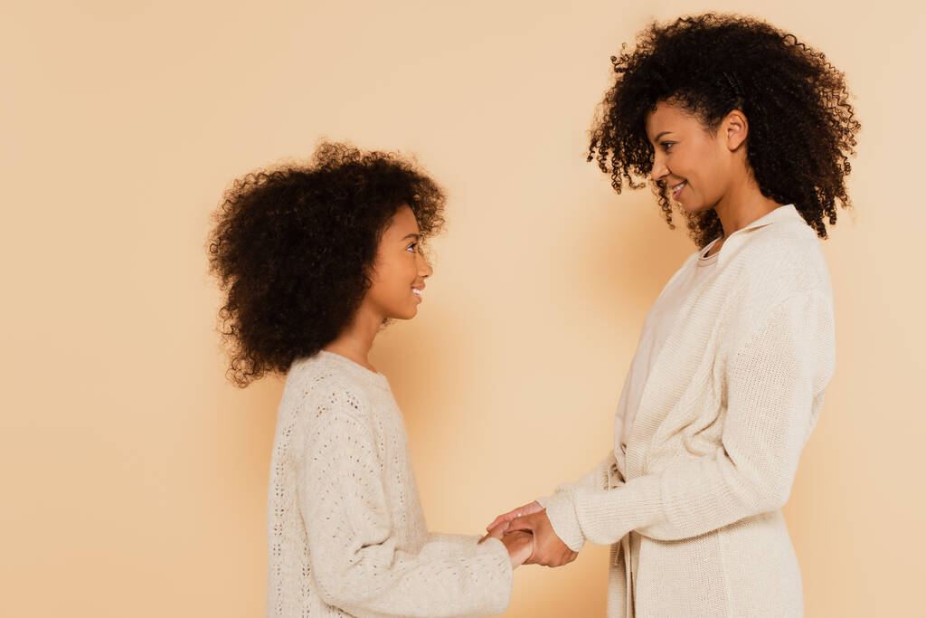 african american preteen daughter tenderly holding hands with mother on beige background - Photo, Image