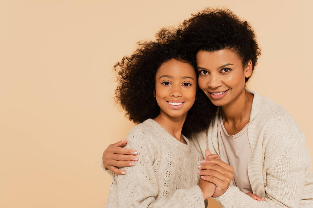 afro-amerikai tinédzser lánya gyengéden fogja egymás kezét és ölelkezik anyjával elszigetelve a bézsen - Fotó, kép