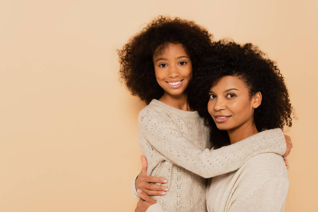 Αφροαμερικανή έφηβη κόρη και ενήλικη μητέρα αγκαλιασμένοι και χαμογελαστοί απομονωμένοι στο μπεζ - Φωτογραφία, εικόνα
