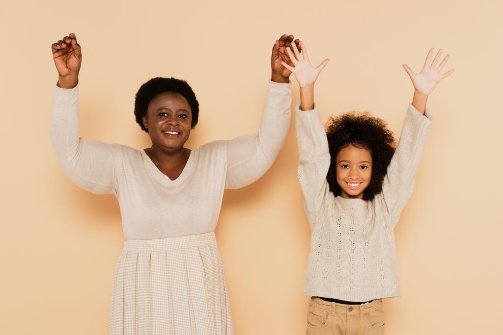 aufgeregte afrikanisch-amerikanische Enkelin und Großmutter halten die Hände hoch und zeigen Handflächen auf beigem Hintergrund - Foto, Bild