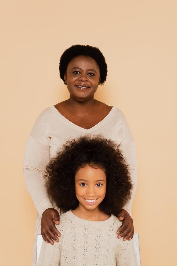 portret van lachende Afrikaanse Amerikaanse kleindochter en grootmoeder op beige achtergrond - Foto, afbeelding