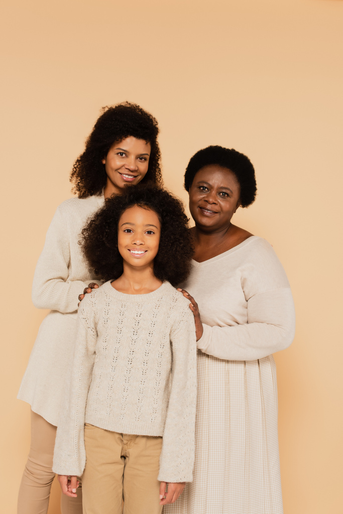 familia sonriente de madre afroamericana, abuela y nieta aisladas en beige - Foto, Imagen