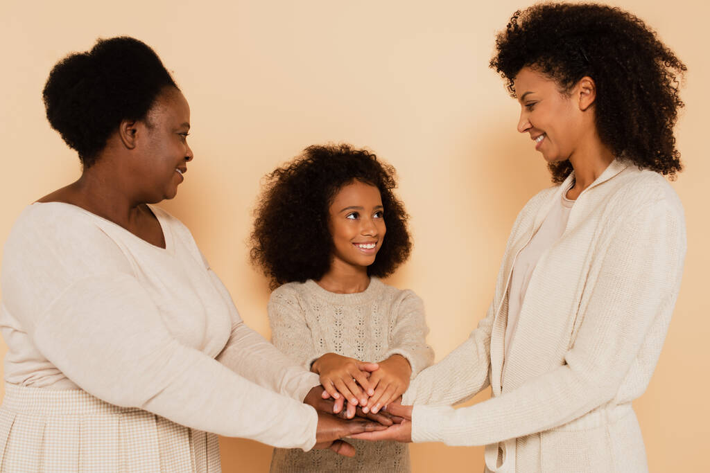 afro-américaine grand-mère, mère, fille se tenant la main sur fond beige - Photo, image