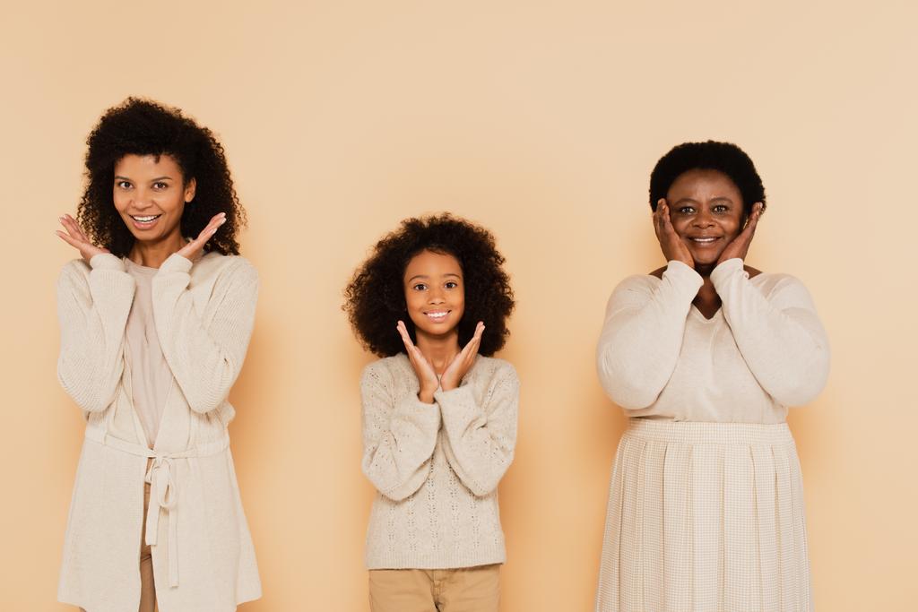 Αφροαμερικανή κόρη, εγγονή και γιαγιά που στέκονται με τα χέρια κοντά στο πρόσωπο σε μπεζ φόντο - Φωτογραφία, εικόνα
