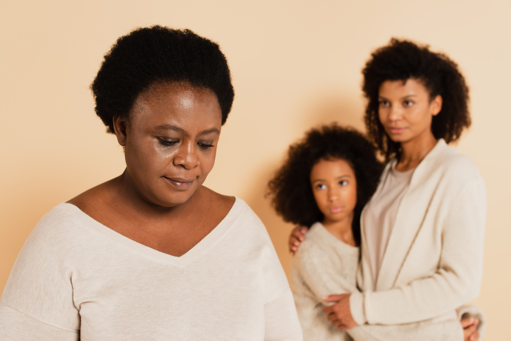 アフリカ系アメリカ人の母親は娘と一緒にベージュを背景に悲しい祖母を見て - 写真・画像