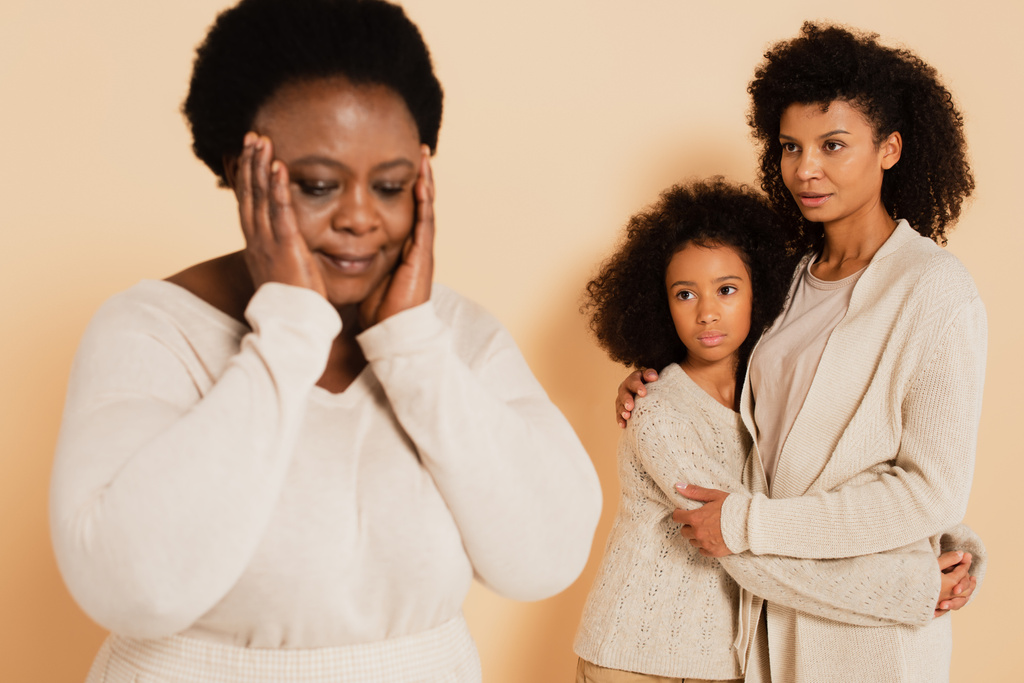 afro-amerikai anya ölelkezik a lányával, és nézi a csalódott nagymama kezét közel fej bézs háttér - Fotó, kép