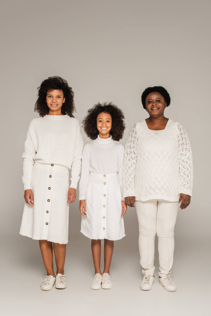 glückliche afrikanisch-amerikanische Mutter, Tochter und Großmutter in weißen Kleidern auf grauem Hintergrund - Foto, Bild