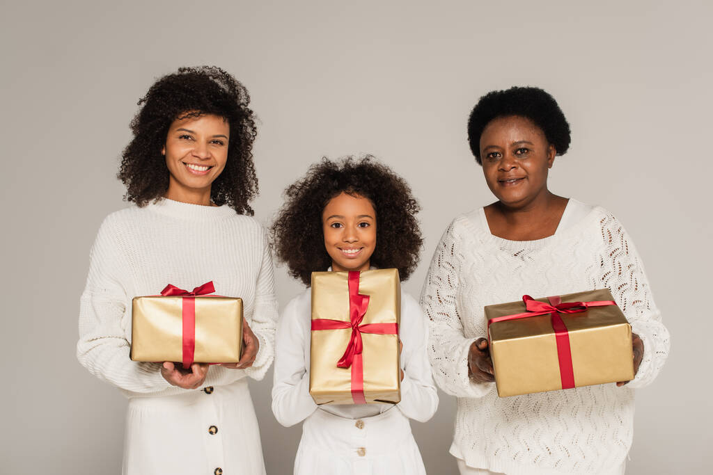 hymyilevä afrikkalainen amerikkalainen äiti, tytär ja isoäiti, jolla on harmaalla eristetyt lahjapakkaukset - Valokuva, kuva