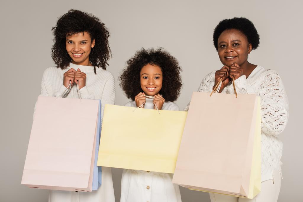 схвильована афроамериканська мати, дочка і бабуся тримають сумки на сірому фоні
 - Фото, зображення