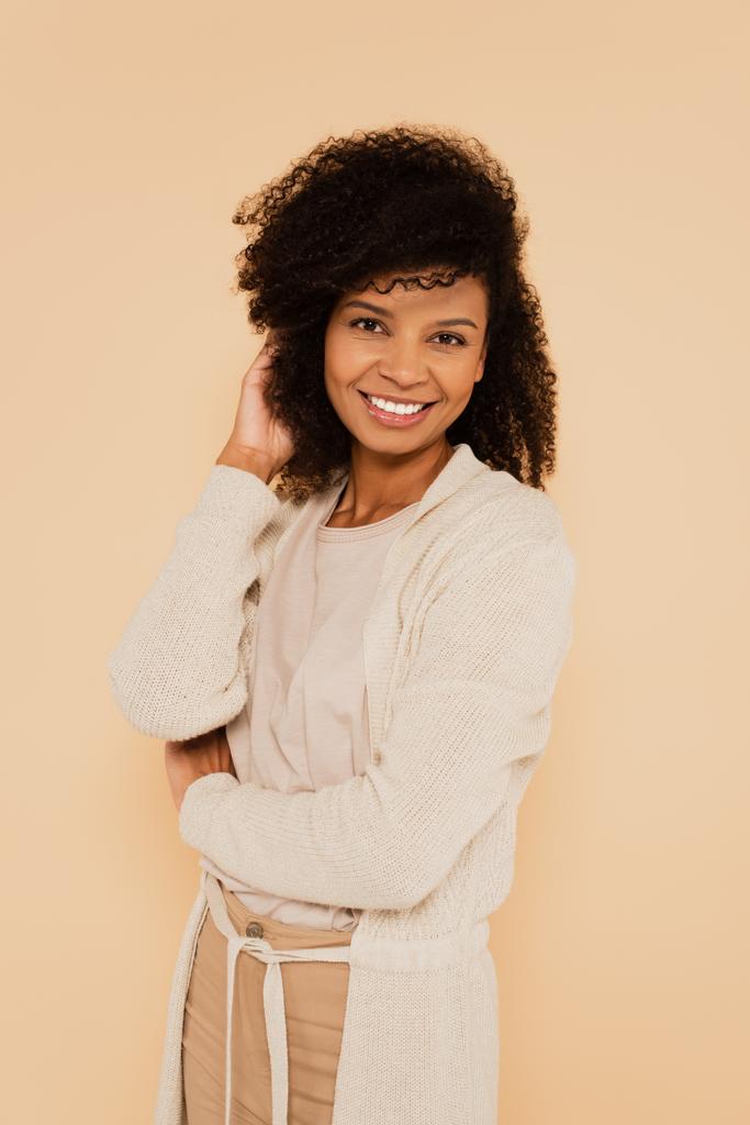 atractiva mujer afroamericana ajustando el cabello aislado en beige - Foto, Imagen