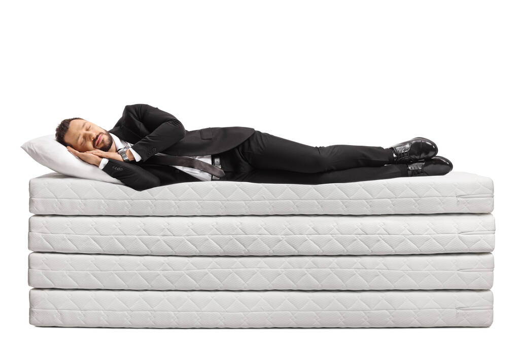 Full length shot van een zakenman in een pak en stropdas slapen op een stapel matrassen geïsoleerd op witte achtergrond - Foto, afbeelding