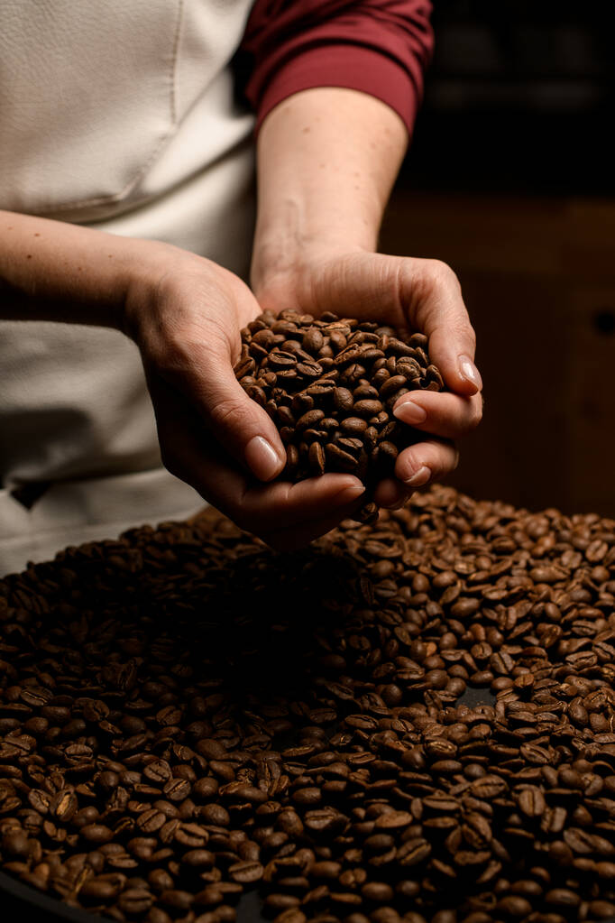 Крупный план женских рук, держащих жареные кофейные зерна над мешком, полным кофейных зерен - Фото, изображение