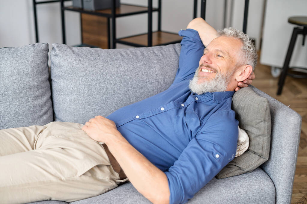 Мужчина средних лет лежит на диване и отдыхает. - Фото, изображение