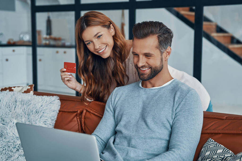 Felice giovane coppia utilizzando il computer portatile e sorridente mentre lo shopping online a casa - Foto, immagini
