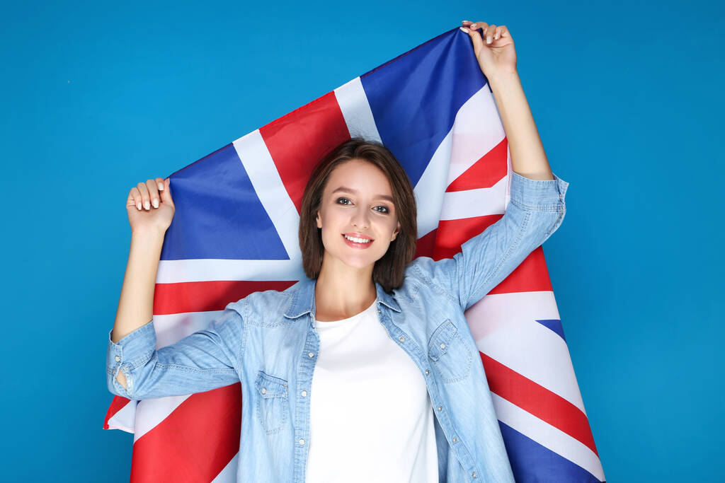 Krásná mladá žena drží britskou vlajku na modrém pozadí - Fotografie, Obrázek