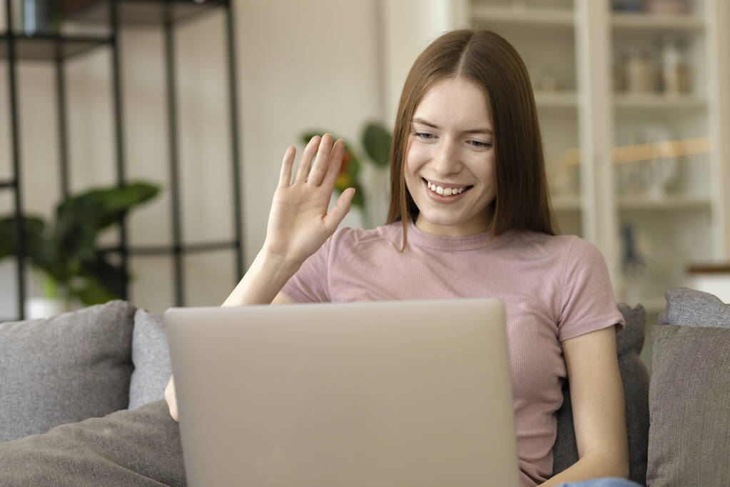 Çevrimiçi iletişim kavramı. Mutlu beyaz kız dizüstü bilgisayar kullanıyor, video konferansında arkadaşlarıyla konuşuyor, evdeki kanepede el kol hareketi yapıyor. - Fotoğraf, Görsel