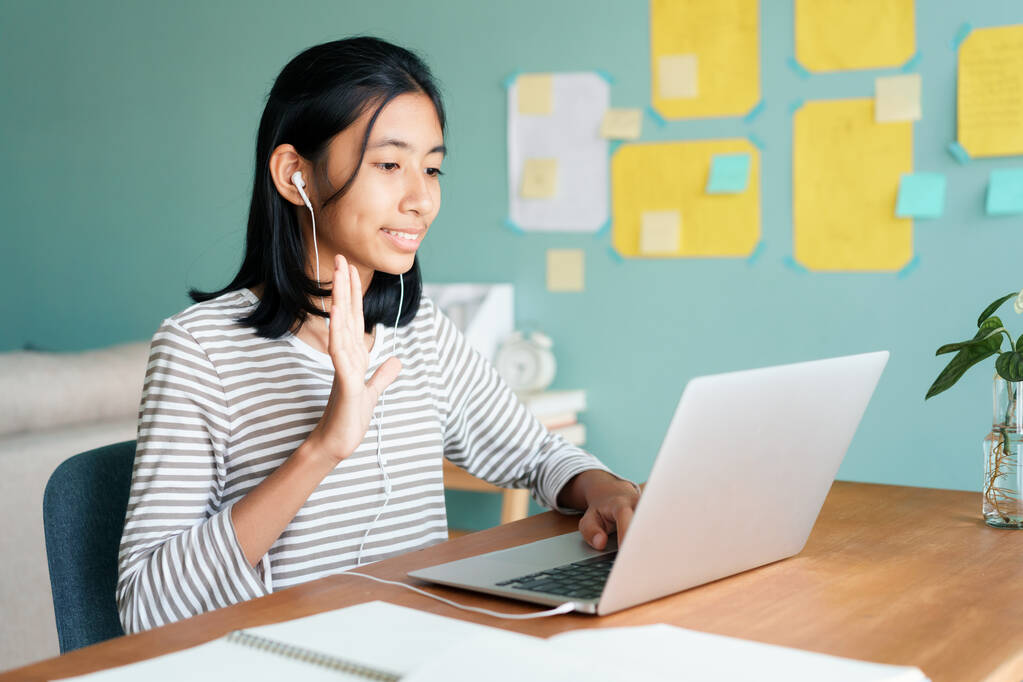 Šťastná asijská dívka mává v pozdravu on-line lektor na tabletu se sluchátky, zatímco sedí na pracovišti doma ráno, Koncepce on-line učení doma - Fotografie, Obrázek
