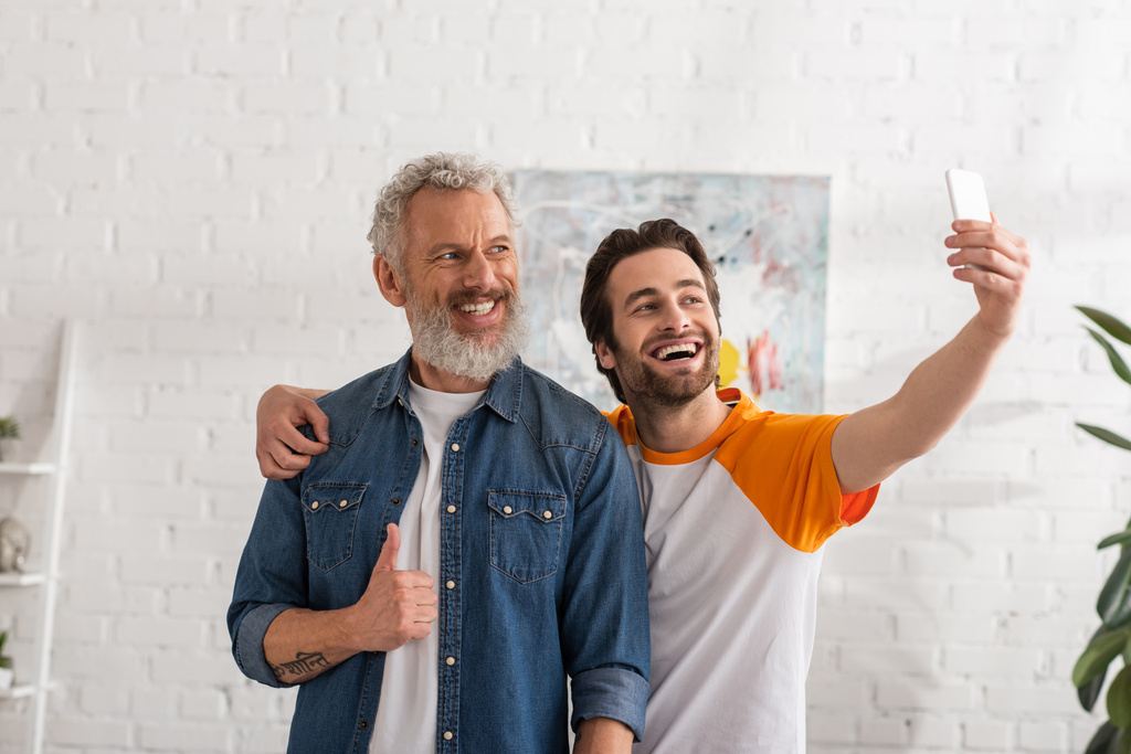 Man showing like gesture while son taking selfie on smartphone  - Photo, Image